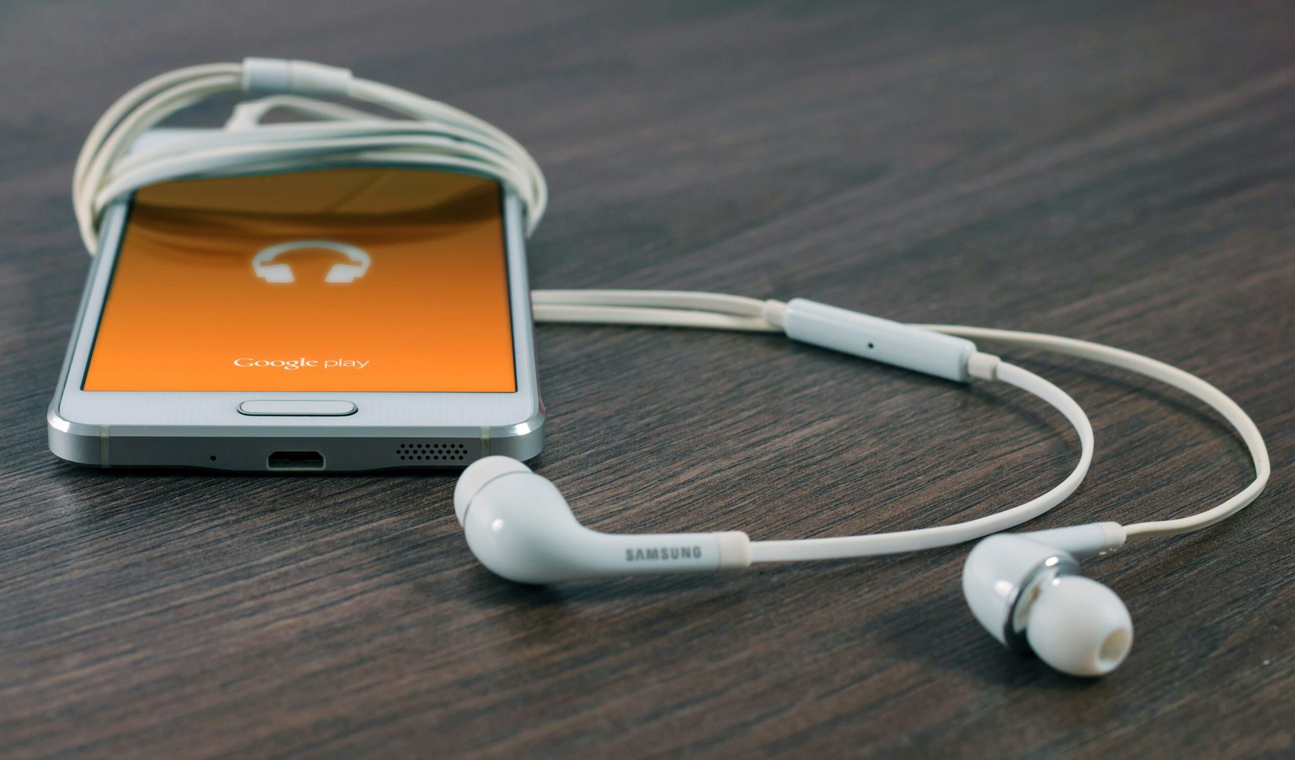 weißes Samsung Android-Smartphone neben weißen Kopfhöhrern auf braunem Brett